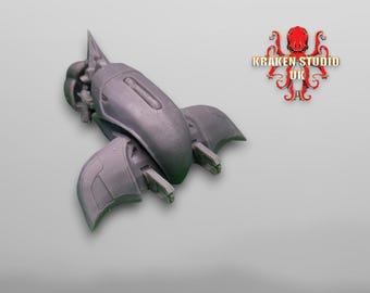 Peut inclure: Modèle gris foncé d'un vaisseau spatial ou d'un véhicule futuriste avec des structures en forme d'ailes et un sommet pointu. Le logo Kraken Studio UK est visible en haut à droite.