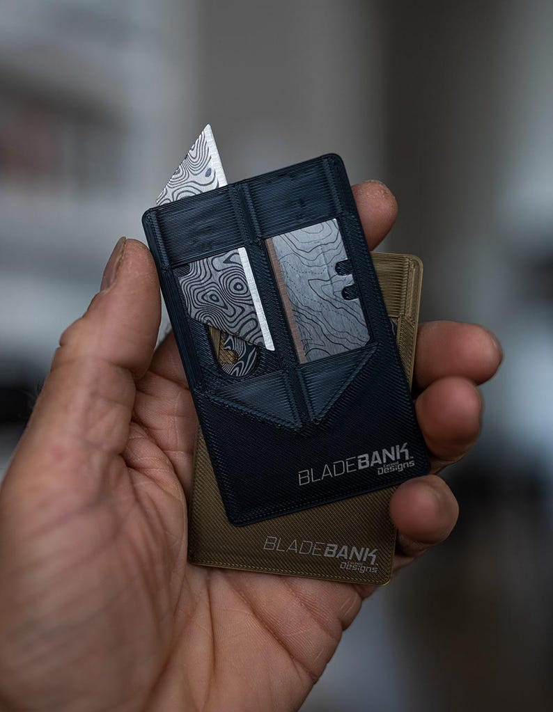 May include: A black card-sized multi-tool with a silver blade and the text "BLADEBANK. Designs" printed on it. The tool is being held in a hand.
