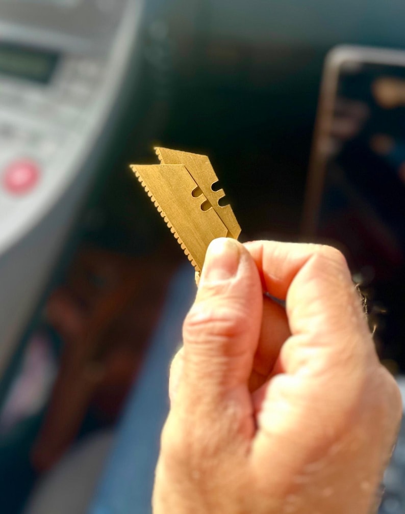 May include: A gold-colored razor blade with a serrated edge.