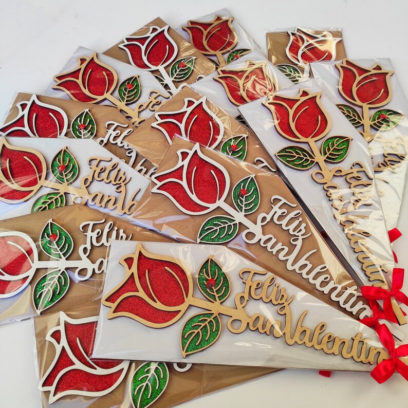 Puede incluir: Un ramo de rosas de madera con detalles de purpurina y el texto "Feliz San Valentin" en cada tarjeta. Las rosas son rojas y las hojas son verdes.