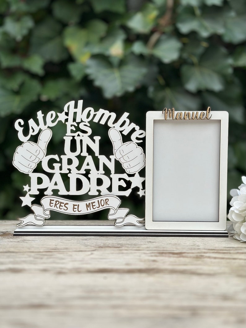 May include: White wooden picture frame with the text "Este Hombre Es Un Gran Padre Eres El Mejor" and a blank space for a photo. The name "Manuel" is written above the photo space.