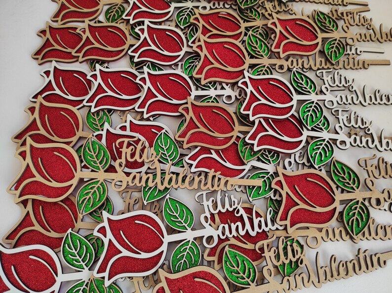 Puede incluir: Un mont&oacute;n de rosas rojas de madera con hojas de purpurina verde y el texto "Feliz San Valentin" en cada rosa.
