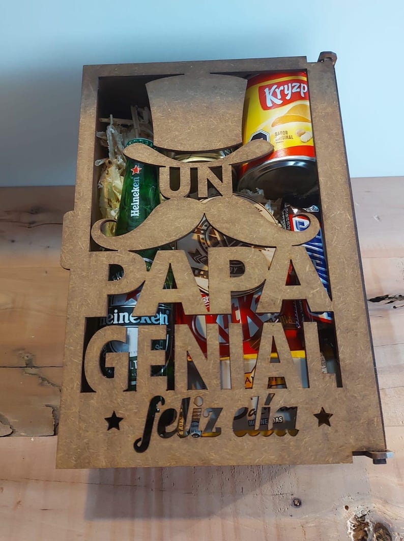 Może przedstawiać: Drewniana skrzynka z wyciętym wzorem, na kt&oacute;rym widnieje napis "Un Papa Genial Feliz Dia" z wąsem i kapeluszem. Skrzynka jest wypełniona r&oacute;żnymi przedmiotami, w tym piwem, chipsami i słodyczami.
