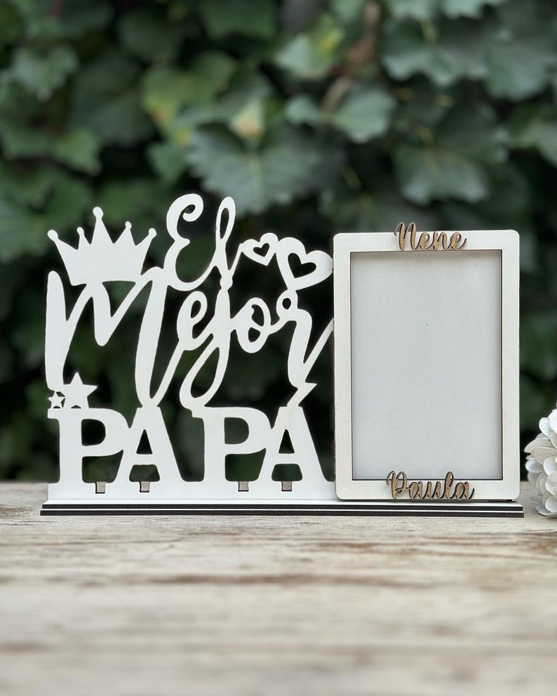 May include: White wooden picture frame with the words "El Mejor Papa" and a crown, heart, and star. The frame has two slots for photos and the words "Nene" and "Paula" are written on the frame.