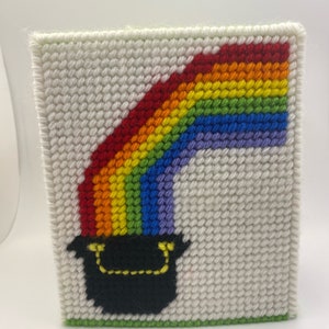 May include: A white canvas with a rainbow and a black pot of gold at the bottom. The rainbow is made of red, orange, yellow, green, blue, and purple yarn. The pot of gold has a yellow handle.