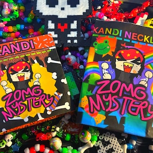 May include: Two colorful Kandi Mystery packs with cartoon graphics and the text "ZOMG MYSTERY" and "KANDI NECKLACE". The packs are surrounded by beaded jewelry in various colors, with a pixelated skull in the background.