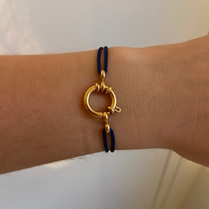 May include: A gold bracelet with a twisted ring clasp and a dark blue cord.