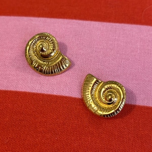 Può includere: Un paio di orecchini dorati a forma di conchiglia. Gli orecchini hanno un design a spirale e sono uno stile classico.