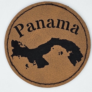 Pode incluir: Um descanso de copo de couro castanho com contorno preto e a palavra "Panamá" impressa em letras pretas. O descanso de copo apresenta uma silhueta preta do país do Panamá.