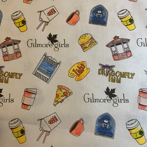 May include: White fabric patterned with various illustrations and text related to the TV show "Gilmore Girls." The design includes coffee cups, pizza slices, burgers, gazebos, and the show's logo. The text includes "Gilmore Girls," "Luke's," and "Dragonfly Inn."