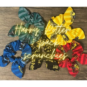 Op de afbeelding: Vijf Harry Potter-thema scrunchies in verschillende kleuren en patronen. De scrunchies zijn gemaakt van stof en hebben een tie-dye-effect. De scrunchies zijn in een cirkel op een houten oppervlak gerangschikt.