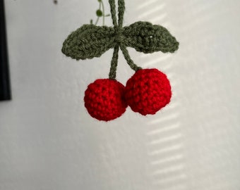May include: Two red crocheted cherries with green crocheted leaves hanging from a string.