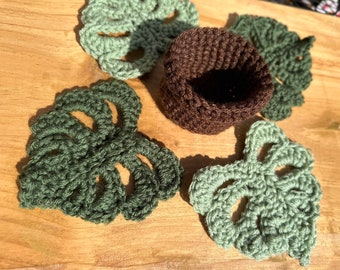 May include: Five crocheted green monstera leaf coasters and a brown crocheted pot holder.