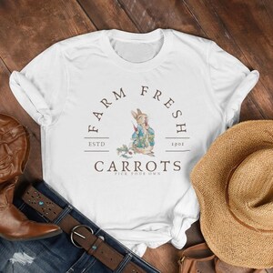 May include: White t-shirt with a brown graphic of a rabbit holding a carrot. The graphic says "Farm Fresh" with "Estd 1901" and "Carrots Pick Your Own".