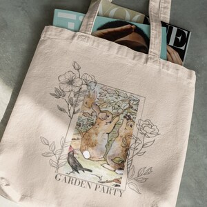 May include: A beige tote bag with a floral design and a picture of rabbits in a garden. The text "GARDEN PARTY" is printed on the bag.