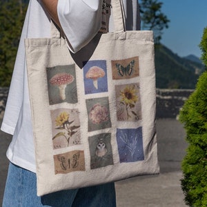 Könnte beinhalten: Eine weiße Canvas-Tragetasche mit einem farbenfrohen Design mit Pilzen, Schmetterlingen, Blumen und einer Eule. Das Design besteht aus neun Quadraten mit verschiedenen Bildern in jedem Quadrat.