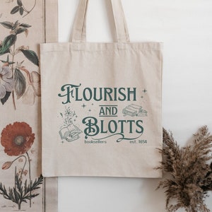 以下が含まれることがあります： 白いキャンバス地のトートバッグに、緑色の文字で「Flourish and Blotts」と書かれています。テキストは飾り文字で書かれており、「booksellers」と「est. 1654」の文字が含まれています。