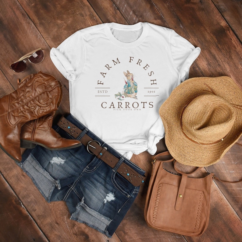May include: White t-shirt with a brown graphic of a rabbit holding a carrot. The graphic says "Farm Fresh" with "Estd 1901" and "Carrots Pick Your Own".