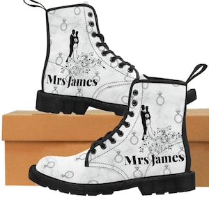 Może przedstawiać: Białe skórzane buty z czarnymi sznurowadłami i czarną podeszwą. Buty mają wzór przedstawiający parę młodą z pierścionkami i napis "Mrs. James".