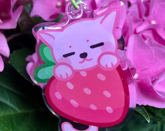 Könnte beinhalten: Ein rosa-weißer Katzenanhänger mit einem rosa Erdbeer-Design. Der Anhänger ist an einem grünen Schlüsselanhänger befestigt.