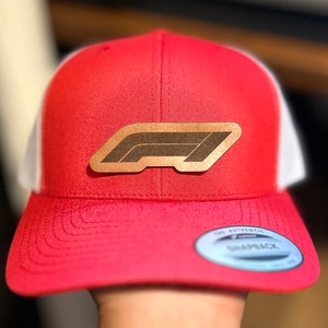 May include: Red and white trucker hat with a brown leather Formula 1 logo patch.