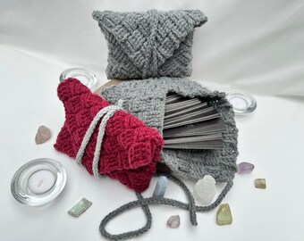 May include: Two crocheted pouches with a textured basketweave pattern. One pouch is dark red with a light grey drawstring, and the other is grey with a flap closure. A deck of black cards with silver edges is partially inside the grey pouch.