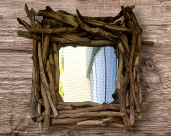 May include: Square mirror framed with natural driftwood, featuring a rustic, textured border in shades of brown and tan. The mirror reflects a view, set against a wooden background. The frame is made of various pieces of driftwood.