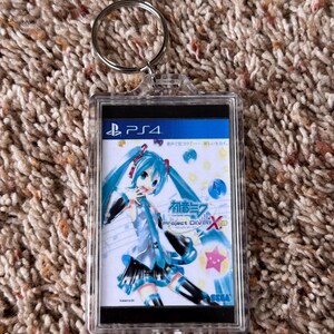 May include: A clear rectangular keychain featuring a colorful anime illustration of a character with blue hair. The keychain has a silver ring and the text "PS4" and "Project DIVA X" are visible.