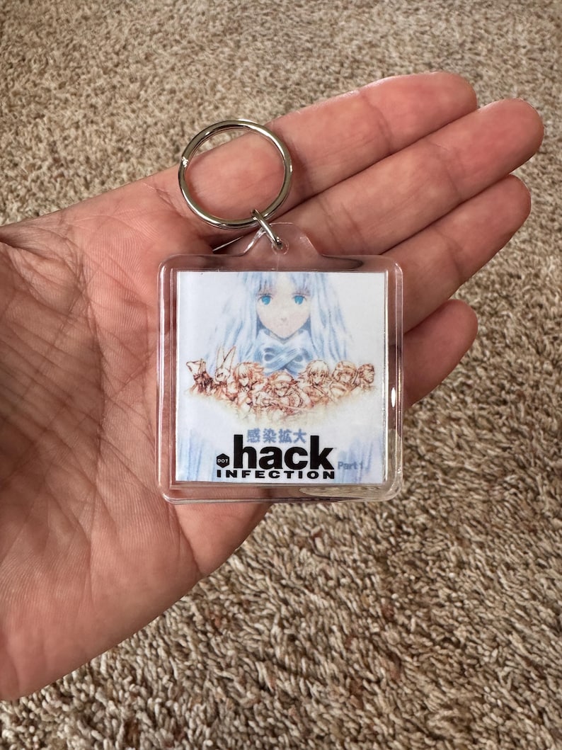 Pode incluir: Chaveiro quadrado transparente com arte em estilo anime. A imagem mostra uma personagem com cabelo comprido azul e um la&ccedil;o azul. O texto "hack INFECTION" &eacute; impresso abaixo, juntamente com caracteres japoneses.