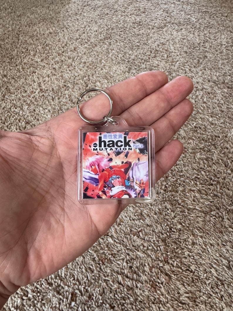 Pode incluir: Um chaveiro quadrado com um anel de metal. O chaveiro tem um gr&aacute;fico colorido com a palavra "hack" em uma fonte estilizada e texto japon&ecirc;s. O gr&aacute;fico apresenta personagens em estilo anime em vermelho, rosa e azul.