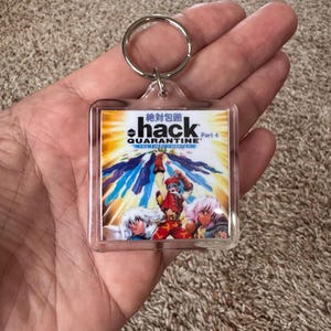 Pode incluir: Chaveiro de acr&iacute;lico transparente com um gr&aacute;fico colorido em estilo anime e o texto "hack QUARANTINE" e caracteres japoneses. O chaveiro tem um anel de metal prateado.