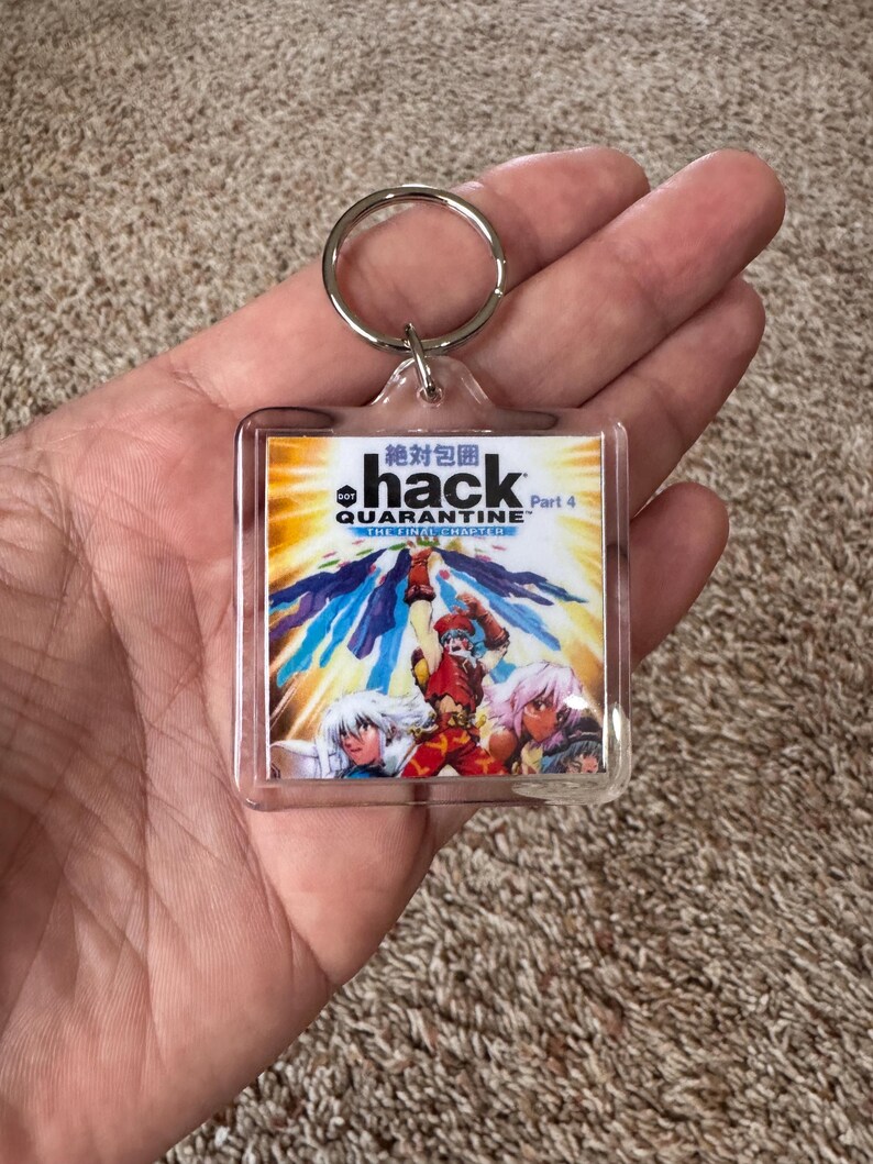 Pode incluir: Chaveiro de acr&iacute;lico transparente com um gr&aacute;fico colorido em estilo anime e o texto "hack QUARANTINE" e caracteres japoneses. O chaveiro tem um anel de metal prateado.
