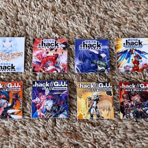 May include: A collection of eight small, square game covers featuring anime-style artwork. The covers display titles like "hack//G.U. Vol. 1 Rebirth" and "hack//Mutation." The color palette includes reds, blues, and oranges, with Japanese text.