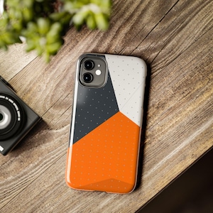 May include: A phone case with a geometric design featuring orange, white, and gray colors. The case has a dotted pattern on the orange and gray sections.