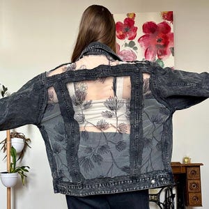 May include: A black denim jacket with a sheer mesh panel on the back featuring embroidered floral designs. The mesh panel is visible through cutouts in the denim.