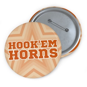 May include: A round button with an orange and beige starburst pattern. The text "HOOK'EM HORNS" is in orange letters with a white outline.