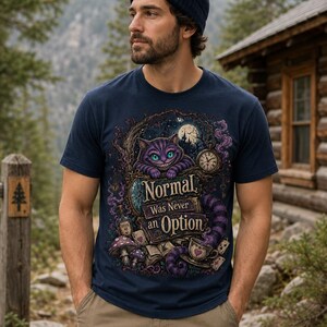 May include: A navy blue short-sleeve t-shirt featuring a graphic print of a purple cat with green eyes, a pocket watch, mushrooms, and a teacup. The text reads, "Normal Was Never an Option." The shirt is paired with a dark blue beanie and khaki pants.
