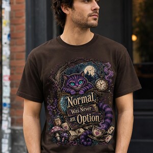May include: A dark brown short-sleeve t-shirt featuring a graphic print of a purple striped cat with green eyes, a pocket watch, mushrooms, and a teacup. The text reads, "Normal Was Never an Option," surrounded by intricate, dark, fantasy-themed illustrations.