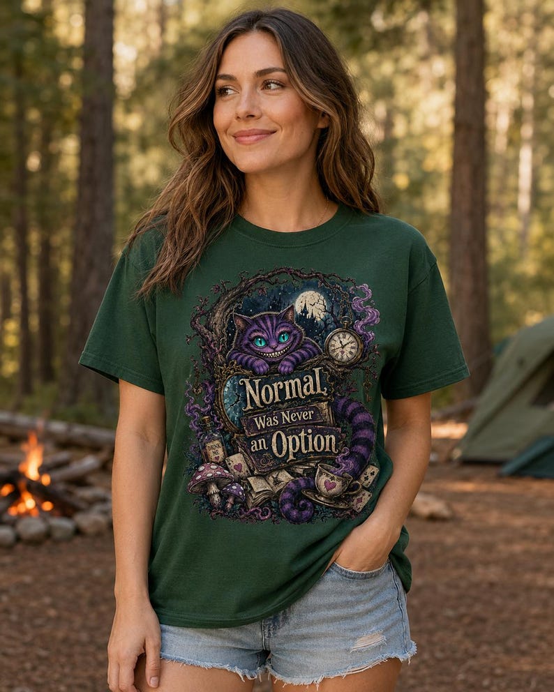 May include: A dark green short-sleeve t-shirt featuring a graphic print of a purple grinning cat, a pocket watch, mushrooms, and playing cards. The text on the shirt reads, "Normal Was Never an Option," surrounded by swirling purple smoke and tree branches.
