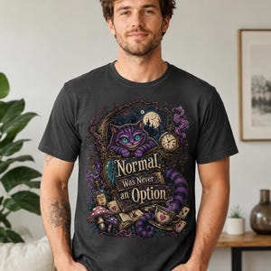 May include: A charcoal gray t-shirt featuring a graphic of a purple striped cat with a wide grin, a pocket watch, a teacup, mushrooms, and playing cards. The text reads, "Normal Was Never an Option," set against a dark, whimsical forest background.
