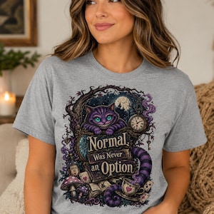 May include: A heather gray t-shirt featuring a graphic print of a purple striped cat with a wide grin, a pocket watch, mushrooms, and playing cards. The text on the shirt reads, Normal Was Never an Option, in a decorative, dark-themed fantasy style.