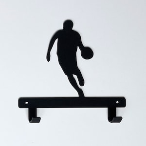 May include: Black metal silhouette of a basketball player with a ball in hand, mounted on a black metal shelf with two hooks.