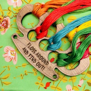May include: Wooden floss organizer with the text "Floss Around and Find Out!" and multiple spools of colorful embroidery floss.