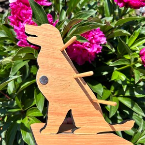 May include: Wooden dog-shaped stand with three dowel rods for holding earrings or other small items. The stand is made of light brown wood and has a black base.
