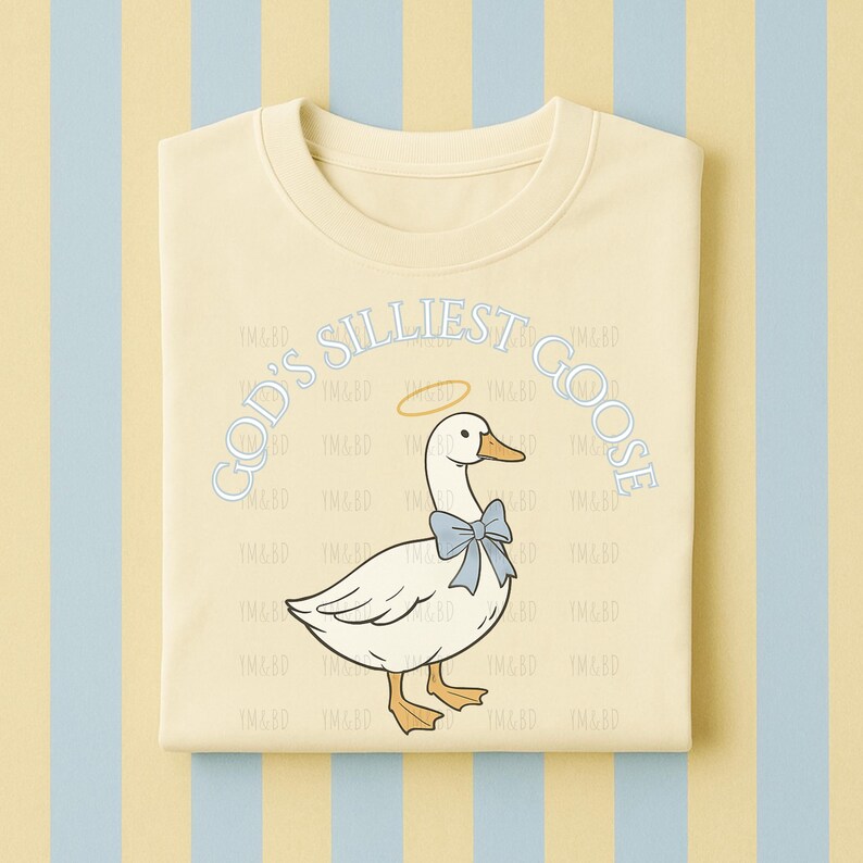 Może przedstawiać: Jasnoż&oacute;łta bluza z napisem "GOD'S SILLIEST GOOSE" w jasnoniebieskim kolorze. Grafika przedstawia białą gęś z niebieską muszką i aureolą. Bluza jest złożona na paskowanym tle.