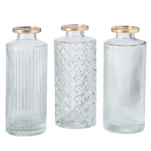 Könnte beinhalten: Drei klare Glasvasen mit goldenen Oberteilen. Die Vasen haben unterschiedliche Texturmuster. Die Vase links hat vertikale Linien, die mittlere Vase ein Diamantenmuster und die Vase rechts diagonale Linien.