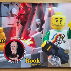 May include: A book cover titled "The Gone Buggo Book" by Steven Gill, featuring a Lego figure with a white t-shirt and an astronaut graphic. The background is a Lego-built scene with a red glow. The Lego figure is holding a black accessory.