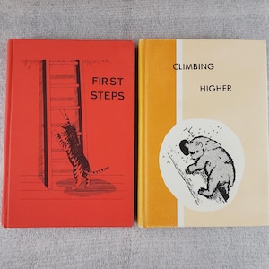 May include: Two vintage children's books. The red book cover features a cat climbing a ladder with the text "FIRST STEPS". The yellow book cover has a bear climbing with the text "CLIMBING HIGHER".