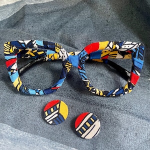 Puede incluir: Gafas y pendientes redondos a juego. Las monturas y los pendientes están cubiertos con una tela colorida con patrones azules, amarillos, rojos y blancos. El fondo es una tela azul.