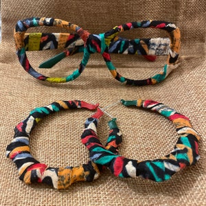Peut inclure: Une paire de boucles d'oreilles créoles en tissu coloré et une paire de lunettes assorties. Le tissu est un mélange de noir, blanc, rouge, jaune et vert.